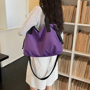 Dettaglio di una grande borsa da viaggio a scacchi viola indossata in un ambiente curato