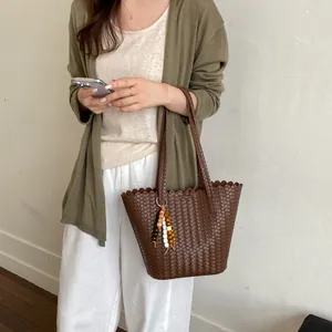 Casual brown woven tote bag with scalloped edge and beaded charm held by model