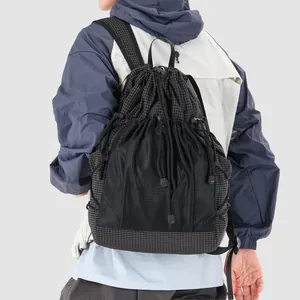 Back view of stylish black grid drawstring backpack worn with an outdoor jacket