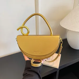 Nahaufnahme einer stylischen goldfarbenen Satteltasche mit markantem gebogenem Griff.