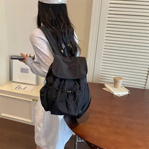 Back view of a black drawstring pleated backpack worn by a model in a cafe setting