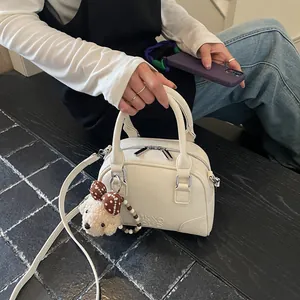 Close-up of white grained leather Boston bag with a cute teddy bear charm and strap.