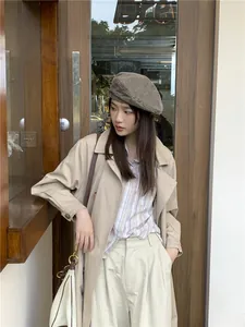 Woman in a stylish retro distressed denim beret with a chic urban trench coat outfit.