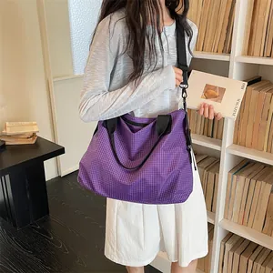 Grande borsa da viaggio a scacchi viola indossata da una modella in una biblioteca
