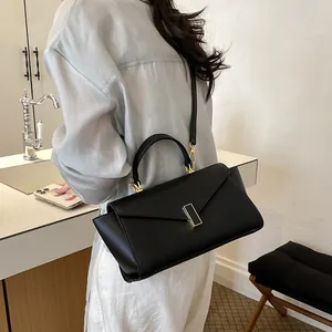 Detail of a minimalist black envelope crossbody bag worn by a model in a modern interior