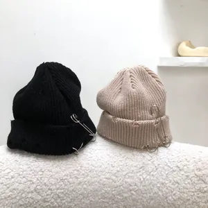 Detailed view of hip hop style distressed knitted beanies with safety pins and rings decor