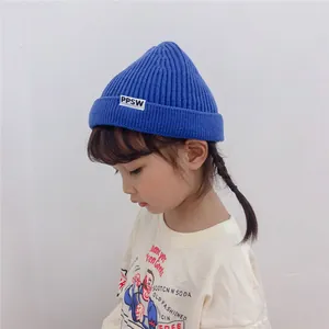 Detail of blue knitted kids beanie with letter patch worn by a child