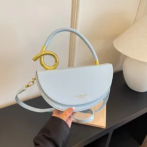 Detail einer hellblauen halbrunden Satteltasche mit goldenem Metallgriff und Trageriemen