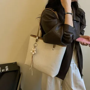 Lifestyle view of large beige woven tote bag with brown trim and floral charm.