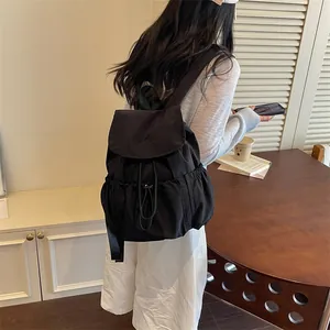 Rear view of a stylish black drawstring pleated backpack worn by a model in a cafe setting.