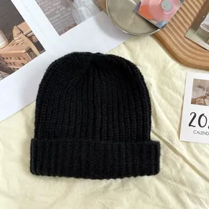Close-up of black coarse knit beanie hat on a cozy cream fabric background for winter