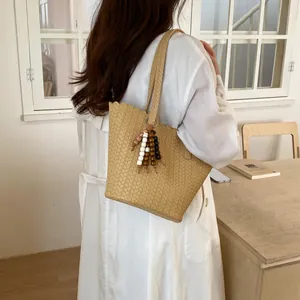 Detail of a beige woven bucket bag with beaded tassel carried by a model in a white dress