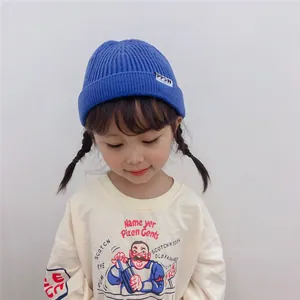 A young girl wearing a cozy blue knitted beanie with a small white letter tag detail
