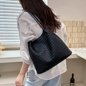 Detail of a minimalist black woven tote bag with long straps worn on shoulder by a model.