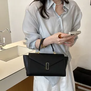 Elegant black leather handbag with gold vertical clasp shown in lifestyle setting