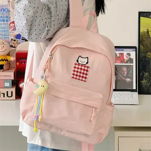 Detail view of a pink backpack with cat embroidery and a moon charm in a cozy room.