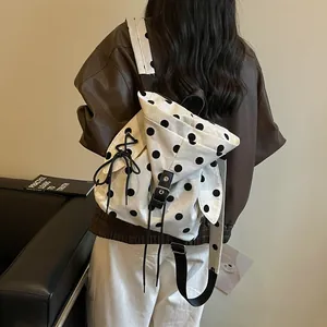 Stylish white canvas backpack with black polka dots worn by a model in a brown jacket