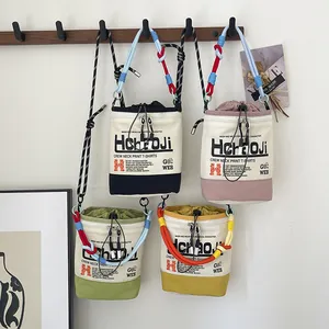 Vier farbenfrohe Canvas-Eimertaschen mit dekorativen Seilriemen an einer Wand hängend