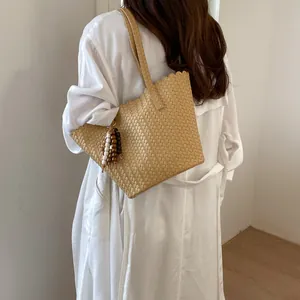 Large capacity retro woven shoulder bag in khaki worn by a model in a long white dress