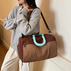 Detailed view of a fashionable brown travel duffel bag with light blue handles carried by a model.