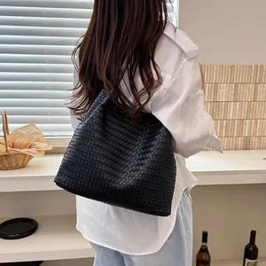Back view of a woman carrying a stylish large black woven tote bag in an indoor cafe