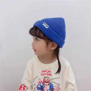 Close-up detail of a blue knit beanie with a white letter label on a cute Asian child