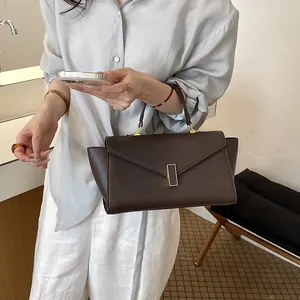Dark brown leather-like handbag with gold clasp held by a woman in a casual setting