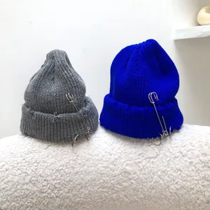 Detailed view of grey and blue distressed knit beanies with safety pin ring accents