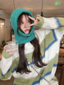 Close-up detail of a green knitted balaclava hood worn by a model in a cozy cafe setting