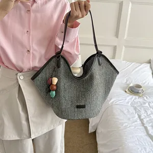 Detailed view of a woven straw tote bag with colorful bead charm held by a person.