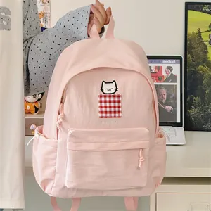 Detail view of a cute pink student backpack with cat embroidery and red check pocket