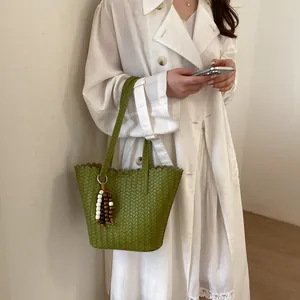 Detail view showing the textured green woven bucket bag with a decorative beaded tassel