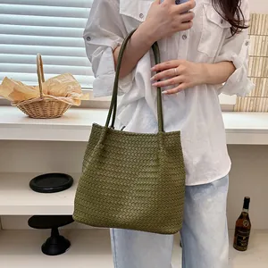 Detailed view of an olive green woven tote bag held by a model in a white shirt.