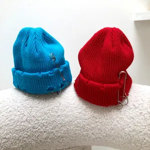 Detail of knit beanies with distressed edges and punk-style metal safety pins and rings.