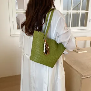 Close-up detail of a large capacity green woven bucket bag on a model's shoulder