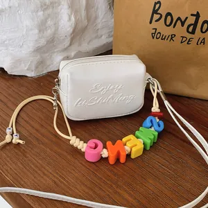 Detail of mini white crossbody bag with colorful alphabet bead strap and embossed text.