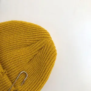 Macro view of yellow knitted beanie featuring safety pin accessory and frayed edge detail