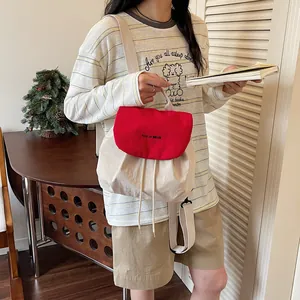 Détail d'un sac à dos léger crème et rouge avec fermeture à cordon et rabat de marque.