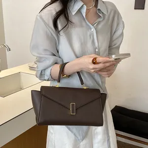 Close-up detail of a classic brown textured handbag held by a model in a stylish indoor setting