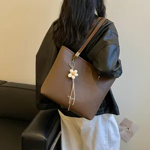 Detail view of a large brown faux leather tote bag with a flower charm on model