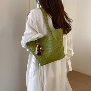 Detail of a green woven shoulder bag with wooden bead charm carried by a model.