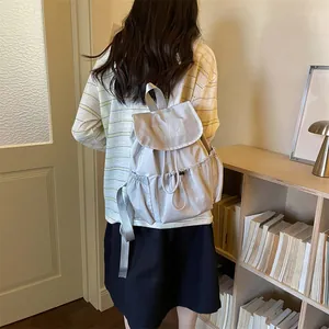 Model wearing the light grey drawstring pleated backpack in a cozy indoor setting