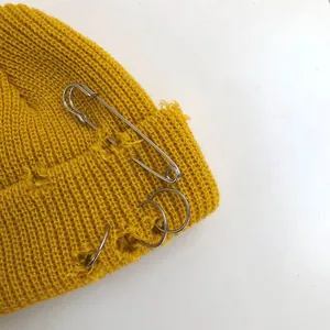 Macro view of yellow distressed knit beanie featuring silver safety pin and metal rings