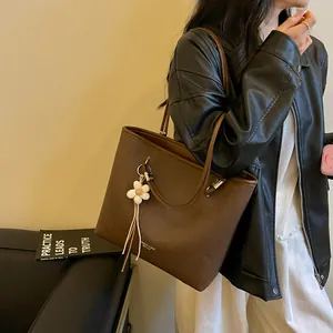 Large brown leather tote bag with flower charm worn by a woman in a leather jacket
