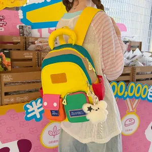 Colorful multi-pocket student backpack with fuzzy bear keychain accessory detail view.