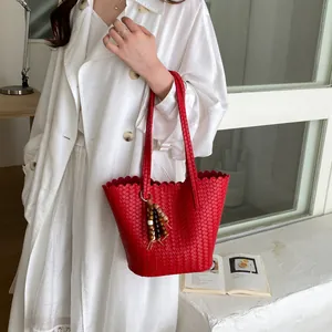 Detailed view of a stylish red woven bucket bag with a wooden bead tassel charm