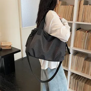 Grande borsa da viaggio a scacchi indossata sulla spalla da una modella in una biblioteca.