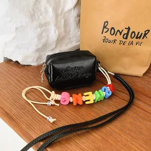Close-up of exquisite black mini crossbody bag featuring a vibrant colorful alphabet bead strap detail.