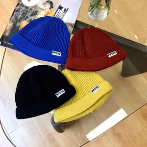 Close-up detail showing four colorful knitted beanies with PPSW logo labels on a glass table