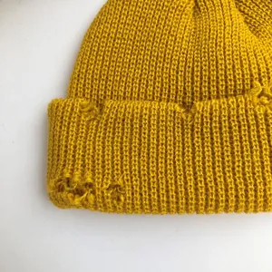 Detailed view of the distressed texture and torn edges on a yellow knitted beanie hat.